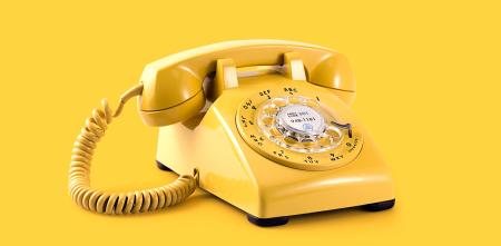 Ein gelbes Wählscheibentelefon vor gelbem Hintergrund.